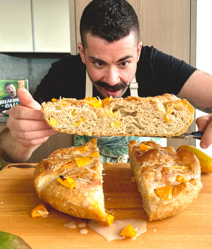 Joe Sasto holding a slice of Foccacia bread with cheese and mangos on a wooden cutting board.