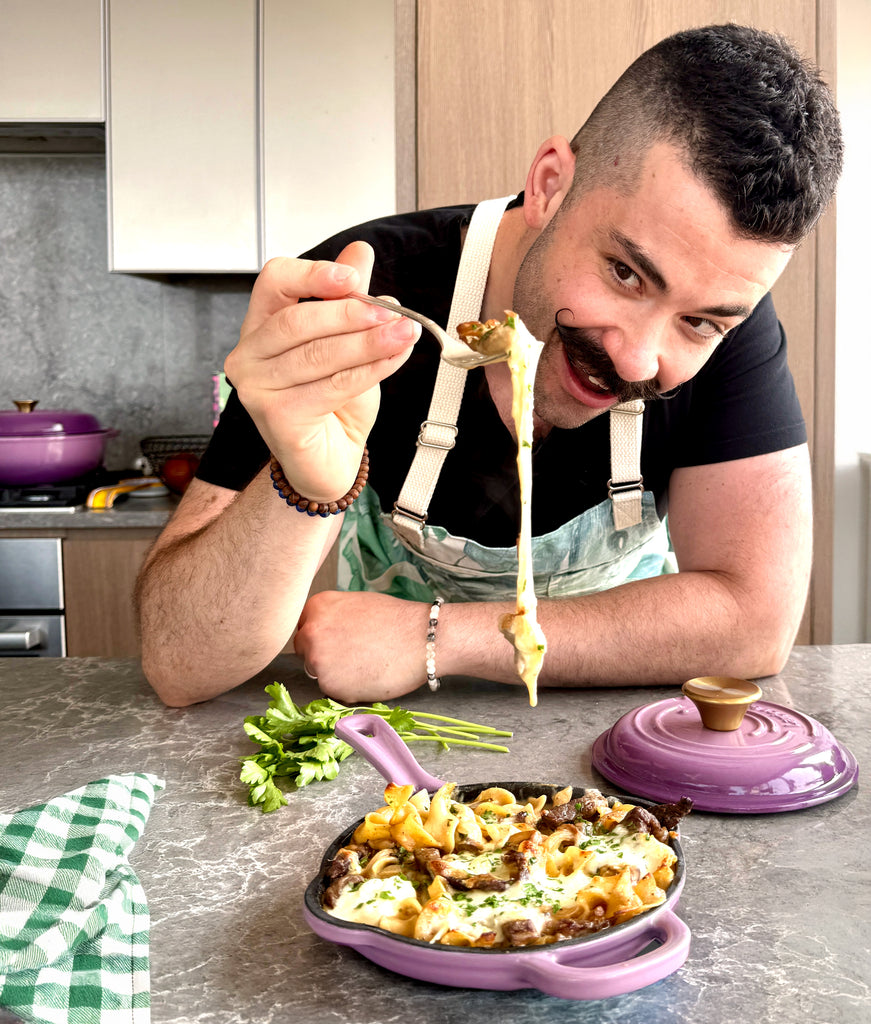 Joe Sasto in a kitchen preparing food, holding a spoon with pasta